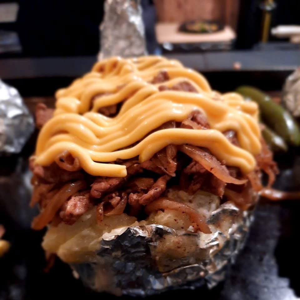 Papa asada rellena de carne con queso amrillo encima